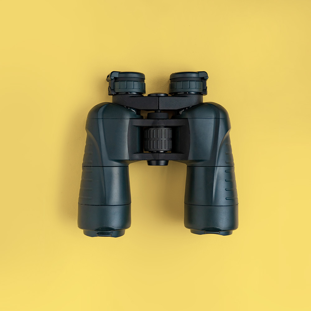 Black binoculars on pastel yellow background