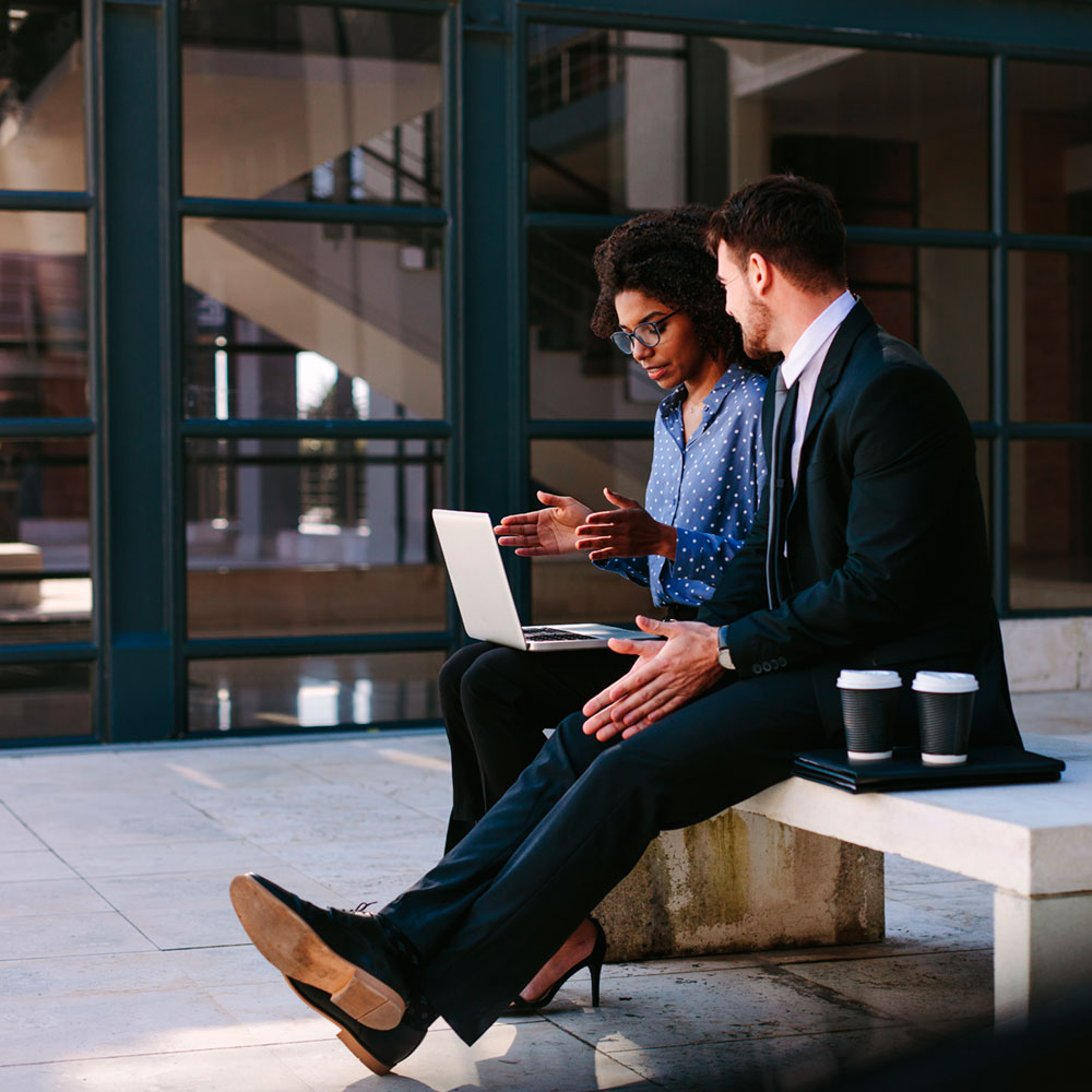 Smart business professionals with laptop and coffee cups talking on a bench